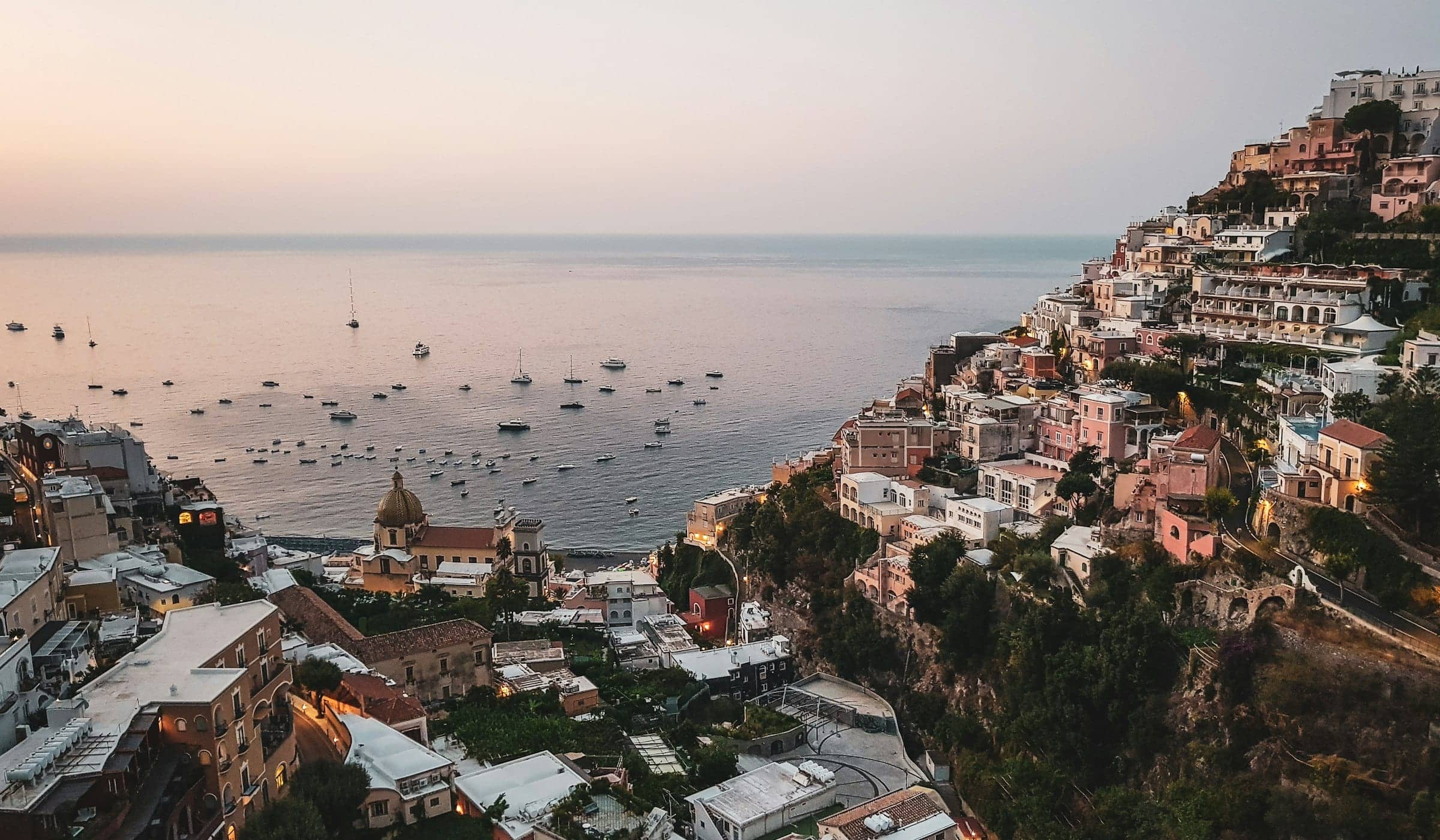 The cliffside town of Positano at dusk, lights coming on above a calm sea