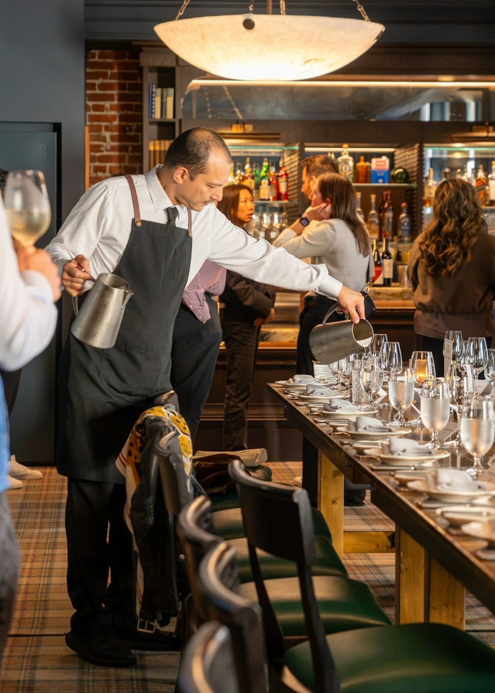 A waiter pouring along a bar set with rows of glasses