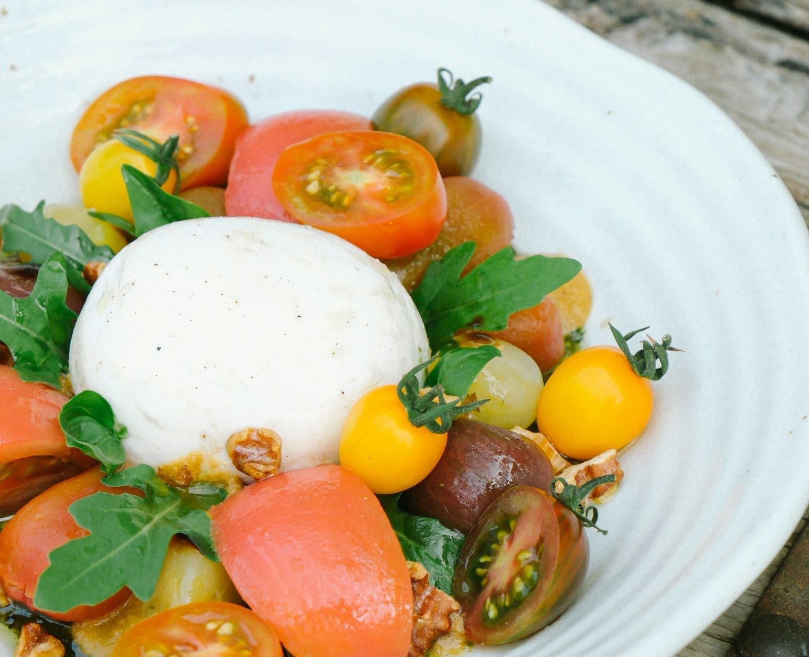 A whole burrata on a plate with heirloom tomatoes and torn basil