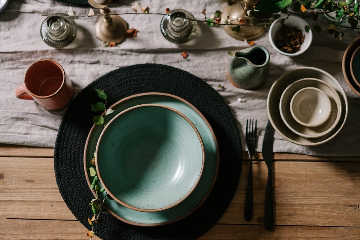 A wooden table laid with linen, dark green ceramics and worn cutlery